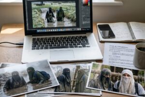 Photo of a messy desk, including laptop and photos.