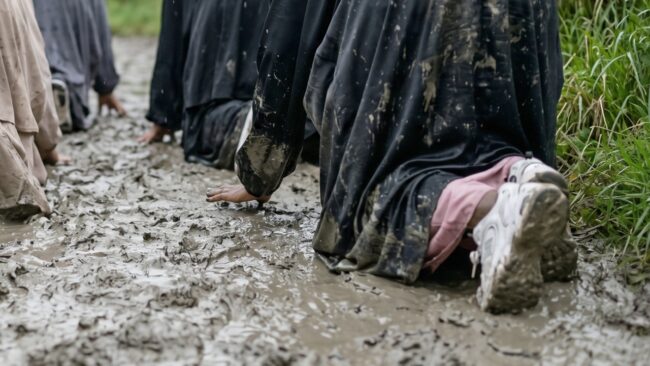 A group of muddy Muslim women crawl under barbed wire during their Trials & Tribulations challenge